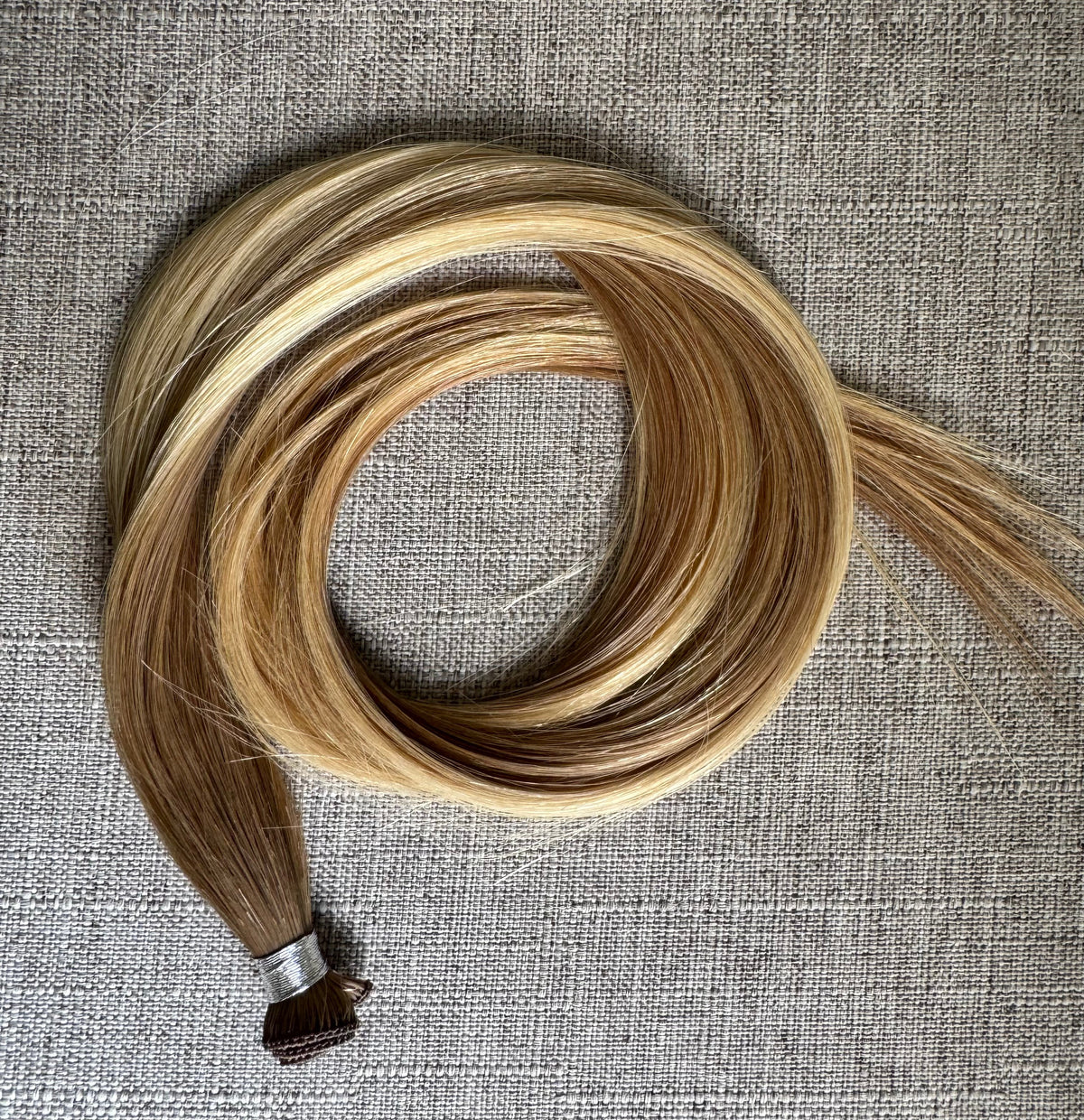 Brooke hand tied hair extension in a warm bronde blend, coiled front view